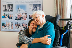 A grandmother embracing her granddaughter in front of a reminisart collage of photos of her life.